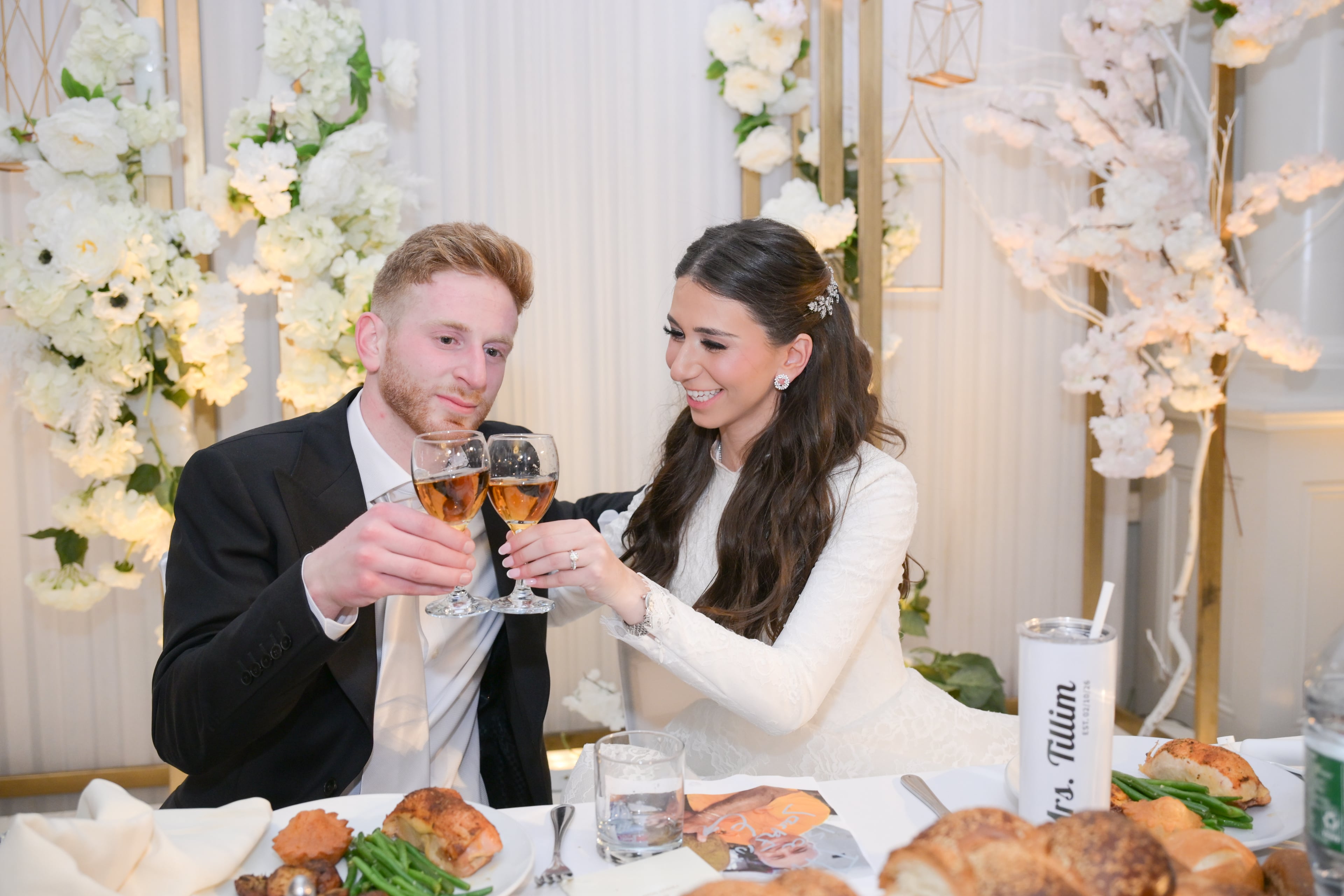 Bride and groom toasting at sweetheart table with white florals